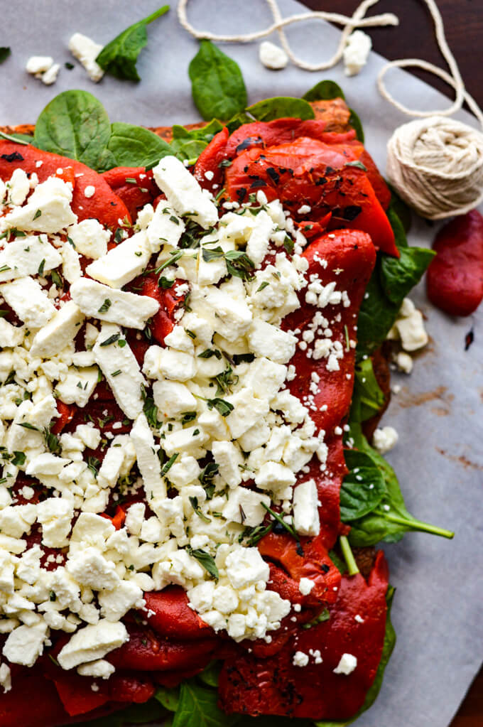 A raw butterflied pork roast with spinach, roasted red peppers and feta cheese on top.