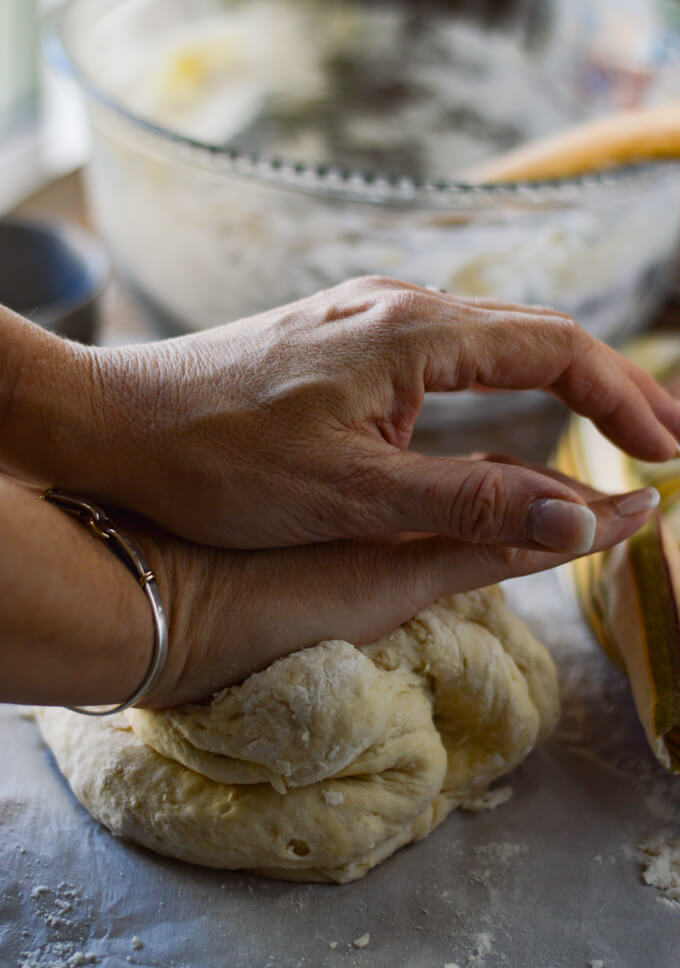Hands are kneading the pizza dough with a glass bowl in the back and a striped napkin beside the dough. 
