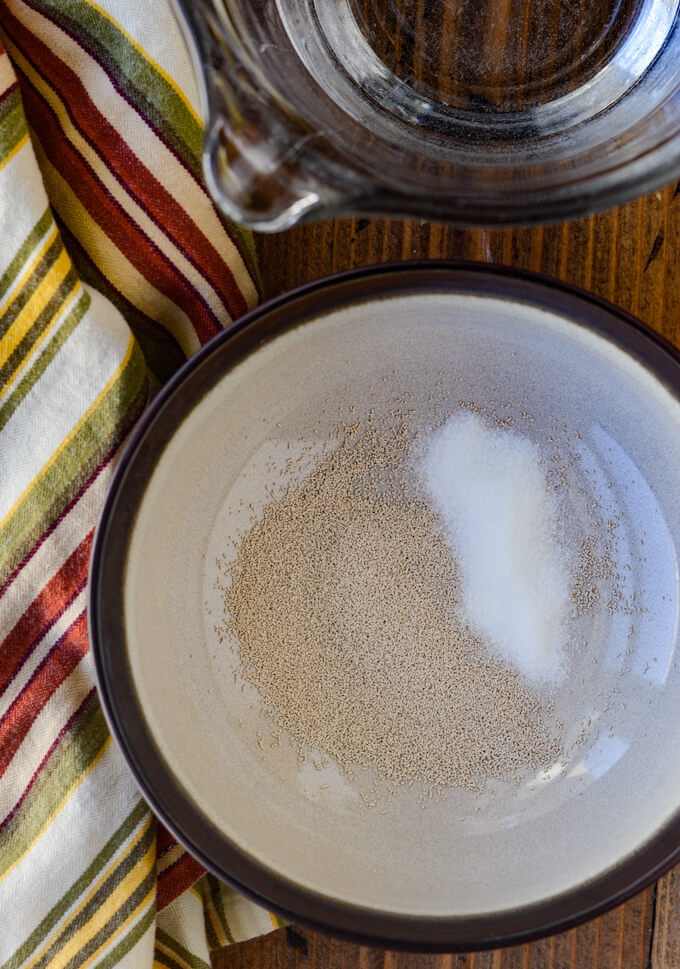 A bowl of yeast with sugar next to a measuring bowl of water and a striped napkin.