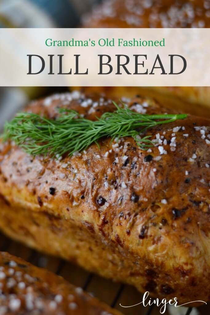 A large loaf of baked dill bread sitting on a wire baking rack with a blue striped napkin in the background.