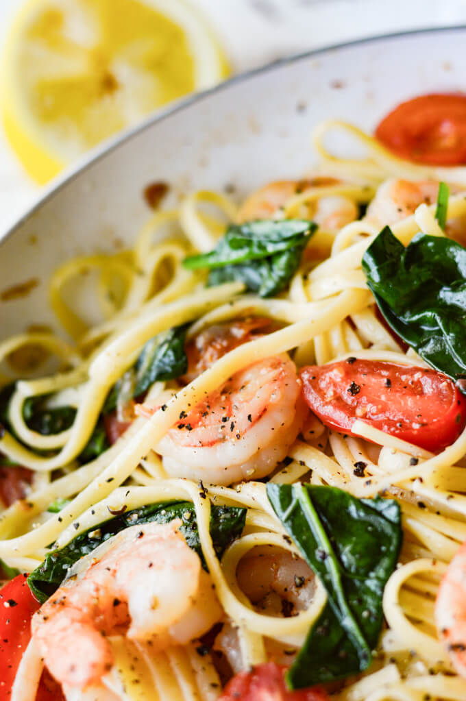A skillet of shrimp scampi pasta with spinach and grape tomatoes.