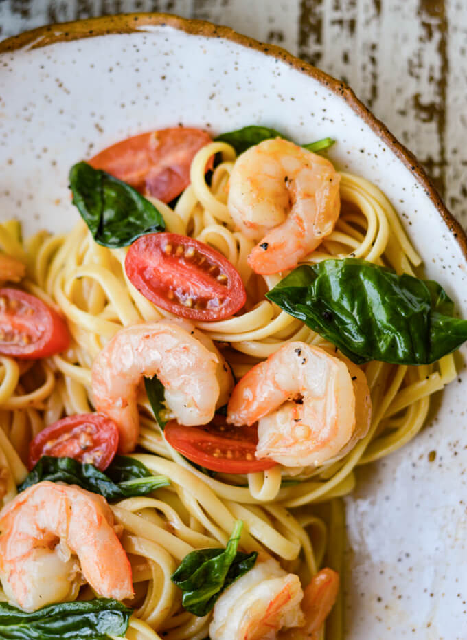 A bowl of shrimp scampi pasta with spinach and tomatoes.
