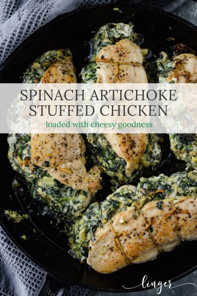 Four fully cooked spinach artichoke stuffed chicken sits in a black cast iron skillet. A gray textured napkin sits next to the pan.