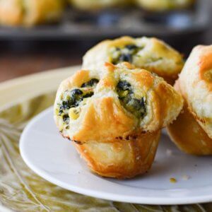 Three spinach stuffed puff pastry appetizers with more appetizers in a muffin tin in the background.
