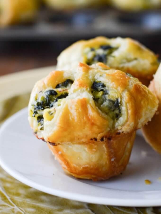 Three spinach stuffed puff pastry appetizers with more appetizers in a muffin tin in the background.
